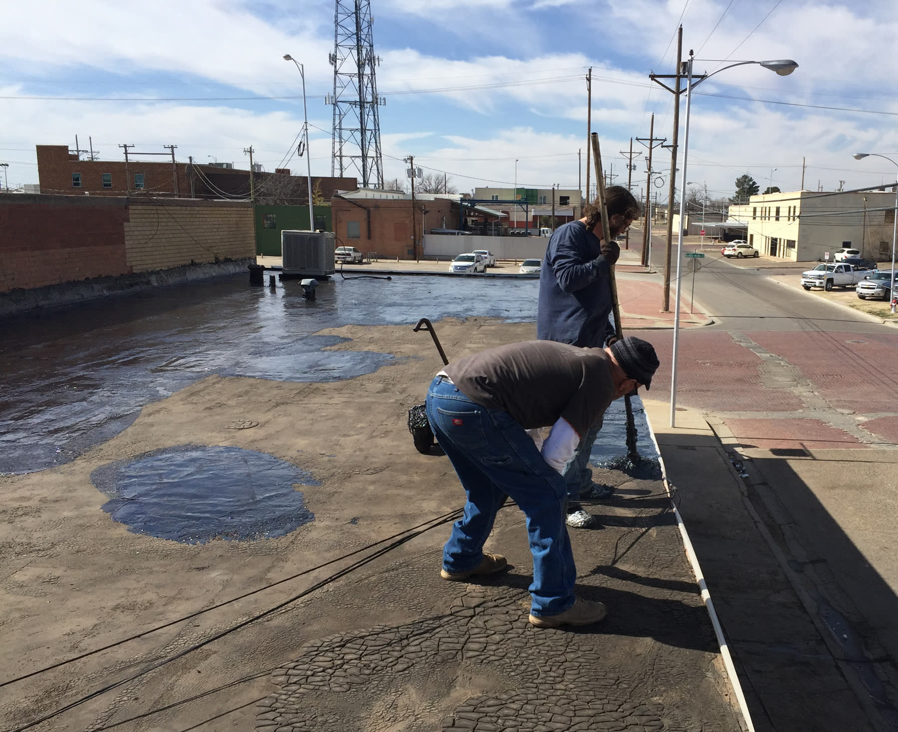 Two roofers working on a flat commercial roof above a city street